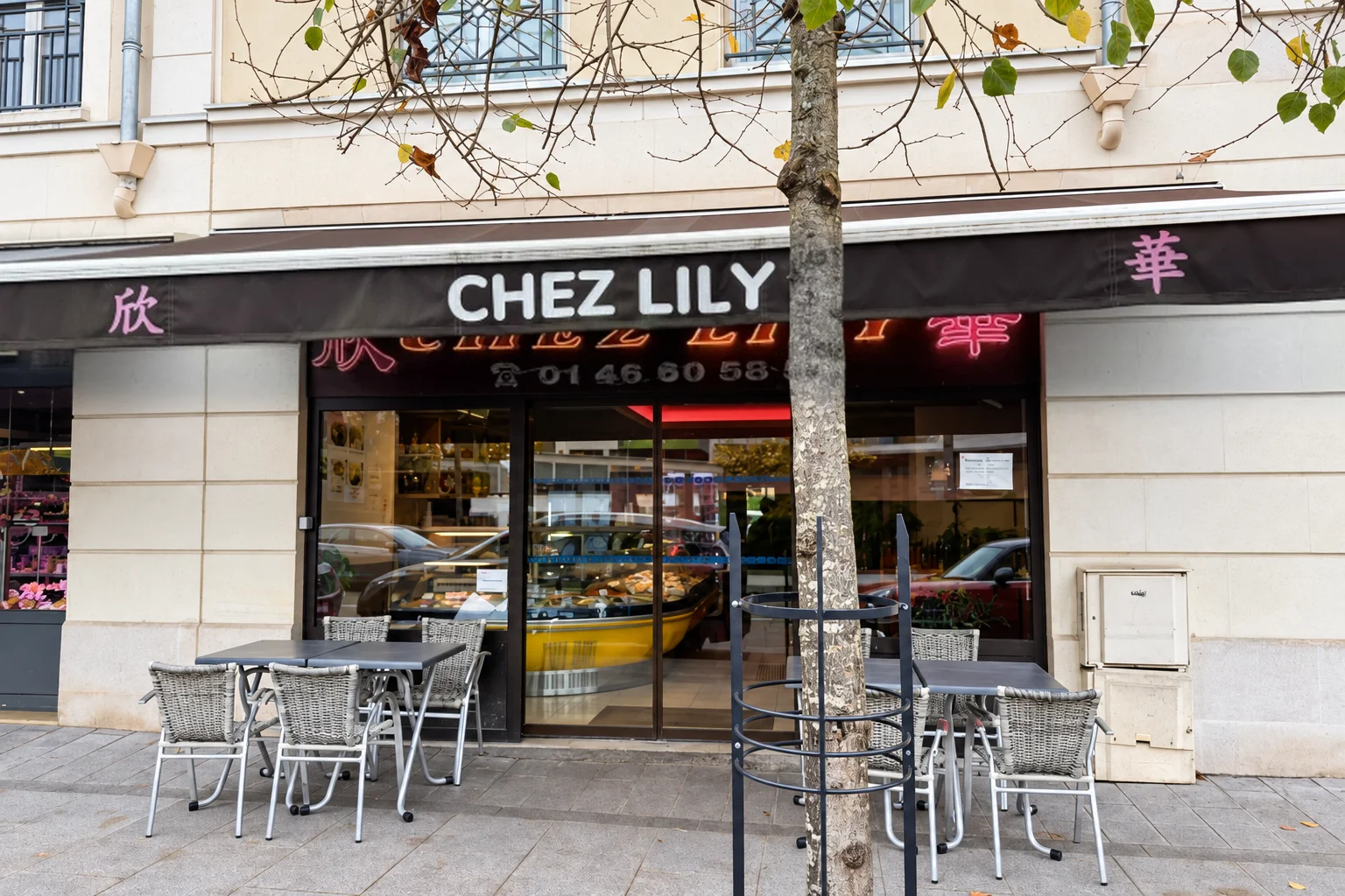 Chez Lily's front: brown awning, neon sign, tables and chairs in front of the window